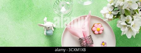 A beautifully arranged table setting for Easter features a pink napkin wrapped around an egg, surrounded by floral decorations and colorful candies, banner Stock Photo