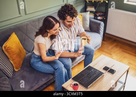 Adult couple is having video call with family. Man and woman sitting at sofa at home and using laptop. Stock Photo