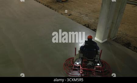 Construction worker using a ride on power trowel to finish concrete slab. Clip Stock Photo