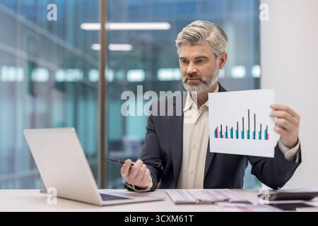 Mature businessman presenting colorful bar chart report during a virtual conference call, discussing financial data and business growth from a modern Stock Photo