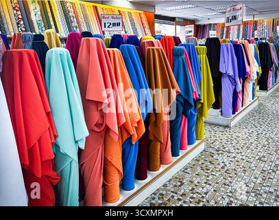 Brightly coloured fabric bolts are displayed in rows inside an asian fabric store, showcasing a variety of indian textiles and patterns Stock Photo