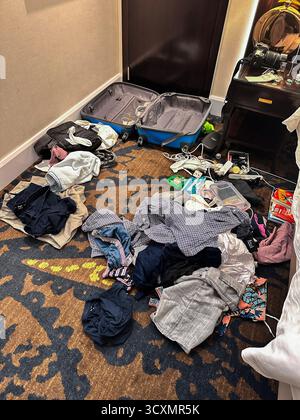 A cluttered Dubai holiday hotel room with an open suitcase and various clothes and electronic items scattered on the floor and around the room Stock Photo