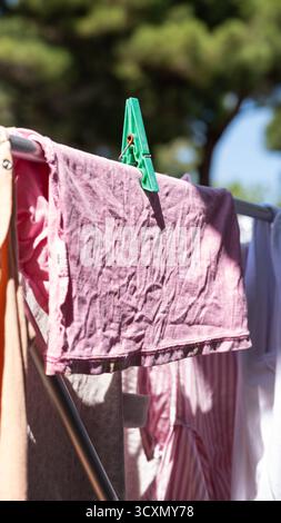 Close-up of pink garment hanging on a drying rack with a green clothespin in bright sunlight. Realistic summer scene symbolizing clean laundry, househ Stock Photo