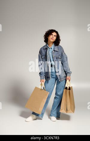 Confident woman in denim, stunning curls, joyfully holding shopping bags. Stock Photo