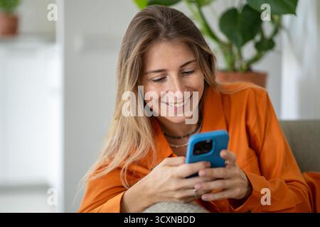 Charming middle-aged woman radiating joy watching funny video while chatting with friends on phone Stock Photo