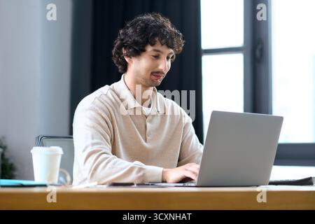 Young man focuses on his laptop, enjoying a productive day in a well lit office. Stock Photo
