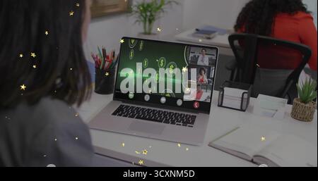 Displaying silver laptop showing split-screen meeting at office desk, with digital currency icons Stock Photo