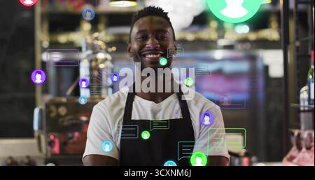 Standing barista wearing t-shirt, black apron behind counter in cafe, with chat bubbles, user icons Stock Photo