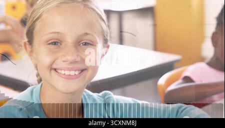 Smiling blonde student in light blue shirt sitting at school desk, with orange chairs, wall decor Stock Photo