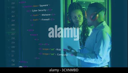Two IT pros reviewing laptop in server room, with racks and code overlay, copy space Stock Photo