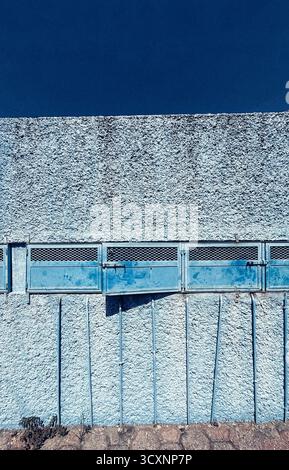 Textured concrete wall with blue metal doors and blue sky, creating an urban industrial scene Stock Photo