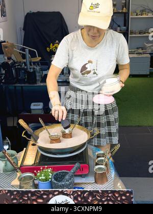 Woman preparing traditional Turkish coffee on sand in a bustling souk market setting with various utensils and equipment visible Dubai old town Stock Photo