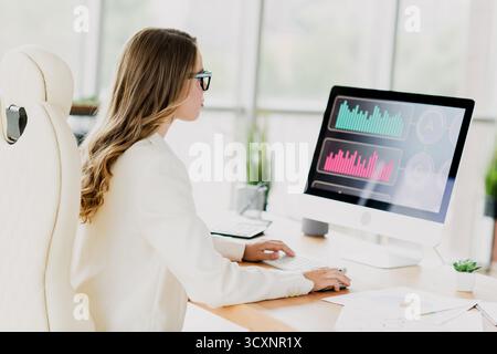 Businesswoman Analyzing Data on a Computer in a Modern Office Setting, Emphasizing Financial and Professional Tasks in a Stylish Interior Stock Photo