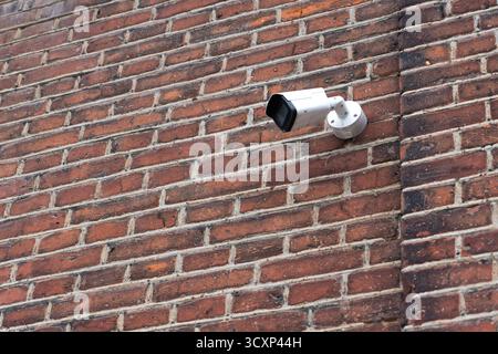 Security surveillance camera mounted on a weathered brick wall. Urban monitoring setup with industrial and rustic textures. Stock Photo