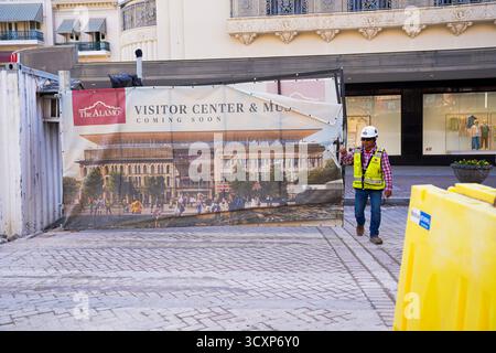 A construction worker walks past a banner showing plans for The Alamo Visitor Center and Museum, part of an ongoing redevelopment in San Antonio Stock Photo