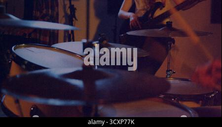 Displaying drum kit with shining cymbals in rehearsal room, with bassist playing bass guitar Stock Photo
