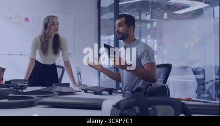 Presenting engineer holding tablet gesturing at drone prototypes in office with whiteboard sketches Stock Photo