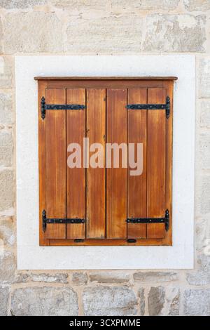 A rustic wooden pair of shutters mounted on a light stone wall, framed by a white stone surround. The warm wood tones and black hinges evoke old-world Stock Photo