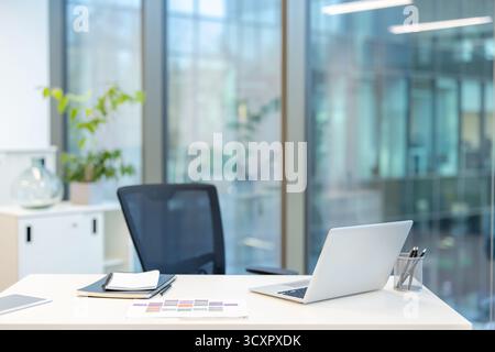 Corporate office workstation providing a professional and quiet environment for working, featuring a modern laptop and stationery on a clean desk, rea Stock Photo