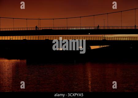 Parallel bridges span the Amsterdam-Rijnkanaal at sunset, cyclists silhouetted on the upper deck with reflections on water in Amsterdam, Netherlands. Stock Photo