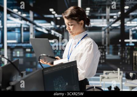 Data center programmer running diagnostic scripts on laptop, examining infrastructure. Server room IT specialist using notebook to evaluate metrics, running tests to maintain system stability Stock Photo