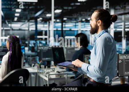 Teamworking engineers in data center installing upgraded server racks systems helped by AI technology. Server room colleagues upgrading enterprise networks equipment using artificial intelligence Stock Photo
