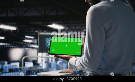 Close up of IT experts using chroma key device to analyze neural networks outputs. Data center admin uses green screen tablet next to colleague reviewing AI visualization in blurry background Stock Photo