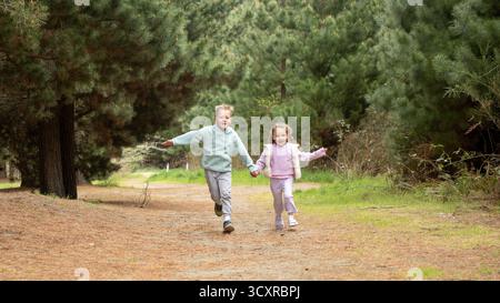 Brother and sister run along path through green forest Stock Photo - Alamy