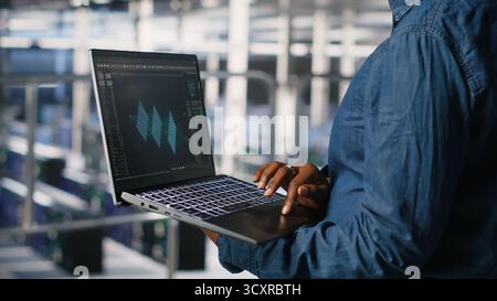 Close up of admin in data center using laptop to monitor neural network LLM visualization. Server hub IT expert overseeing rigs powering machine learning processes using notebook Stock Photo