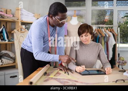 Two sewing workshop workers draw patterns on electronic tablet Stock Photo