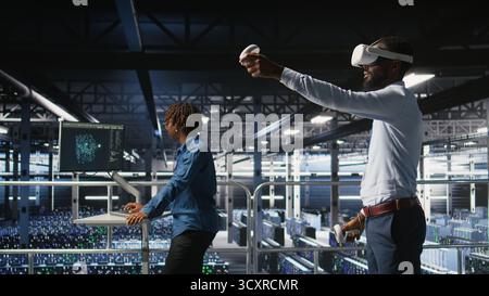 Engineer using VR headset in data center to update server tech, configuring equipment using software tools. Server hub employee reviewing hardware analytics using virtual reality, Stock Photo