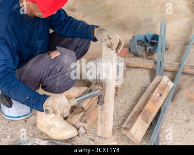 Construction worker removing nails from wooden plank using a hammer claw at building site. Stock Photo