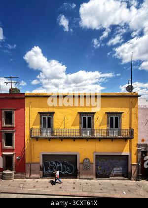 Colorful street view with vibrant yellow building and a person walking under a bright blue sky with scattered clouds Stock Photo