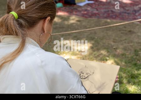 A young woman artist drawing a portrait of a man outdoors on a sunny day in the park, creative process, sketching, fine art Stock Photo