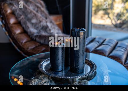 Black candles burning flame on silver pewter platter on glass table next to leather lounge chair Stock Photo