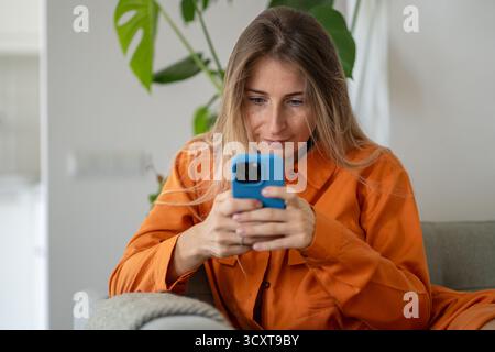 Excited middle-aged woman actively typing and enthusiastically looking at smartphone screen Stock Photo