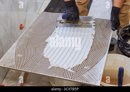 Worker uses trowel to spread adhesive on large tile ready for installation at building site. Stock Photo