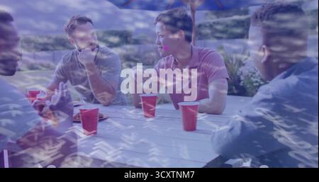 Laughing four friends sitting around picnic table in backyard patio under umbrella, with red cups Stock Photo