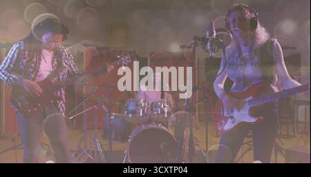 Performing three musicians playing bass, drums and electric guitar while singing into mic in studio Stock Photo