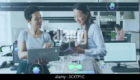 Reviewing code two women collaborating at desk in open-plan tech office, with laptop and tablet Stock Photo