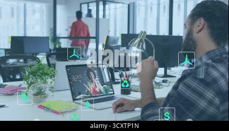 Typing bearded man joining call at open-plan office desk, with laptop plant monitors, copy space Stock Photo