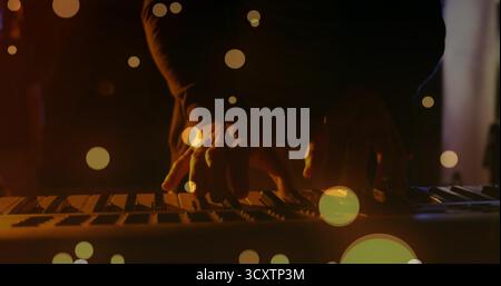 Pressing musician fingers in dark shirt playing keyboard under amber stage light, bokeh overlay Stock Photo