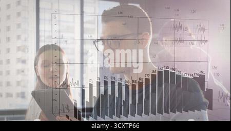 Analyzing colleagues in business casual viewing tablet at office window, with charts and eyeglasses Stock Photo