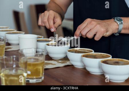 barista or q grader performing coffee cupping to evaluate aroma and flavor quality, professional coffee tasting process with multiple cups on wooden t Stock Photo