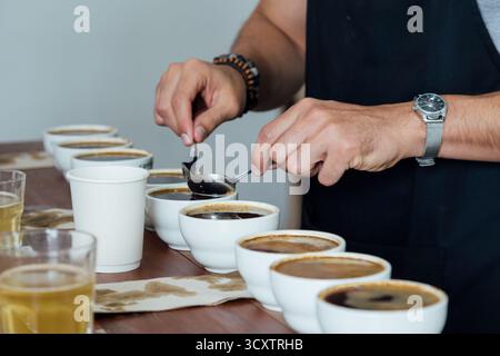 barista or q grader performing coffee cupping to evaluate aroma and flavor quality, professional coffee tasting process with multiple cups on wooden t Stock Photo
