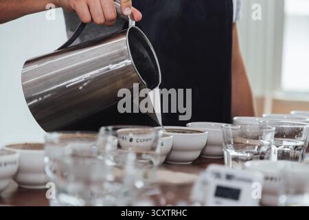 barista or q grader performing coffee cupping to evaluate aroma and flavor quality, professional coffee tasting process with multiple cups on wooden t Stock Photo