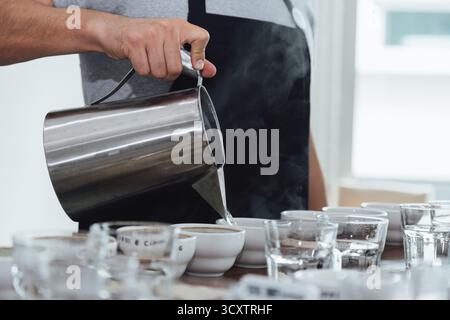 barista or q grader performing coffee cupping to evaluate aroma and flavor quality, professional coffee tasting process with multiple cups on wooden t Stock Photo
