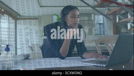 Analyzing code overlay, software engineer wearing blazer at home office with laptop documents, pen Stock Photo