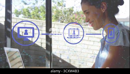 Woman in blue blouse viewing icons connecting laptop desktop smartphone at home office, copy space Stock Photo