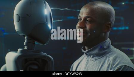 Close Up of Guy Smiling Warmly While Looking Futuristic Robot With AI and Shiny Details. Positive Interaction Between Humans and AI, Trust, Friendly Future of Robotics and Technological Partnership. Stock Photo